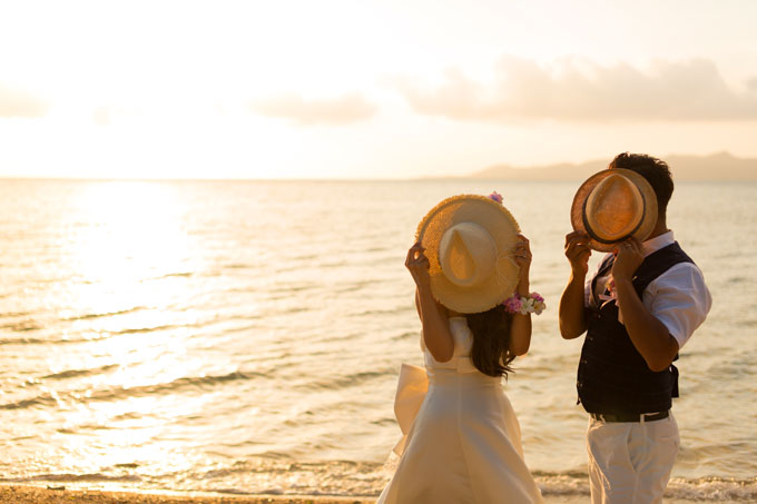 ペアグッズの麦わら帽子を持って沖縄のサンセットビーチで撮影